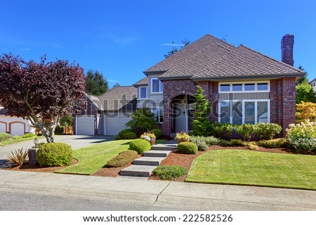 Big luxury house with tile roof and brick wall trim. Walkway decorated with flower pots