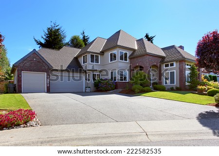 Big luxury house with tile roof and brick trim. View of garage with driveway. Beautiful front yard landscape