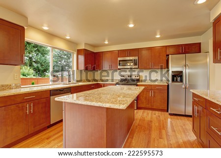 Kitchen with bright wooden cabinets, steel appliances and granite tops. Kitchen room has kitchen island
