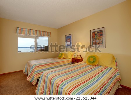 Light tone bedroom with two single beds in cheerful striped bedding with yellow pillows