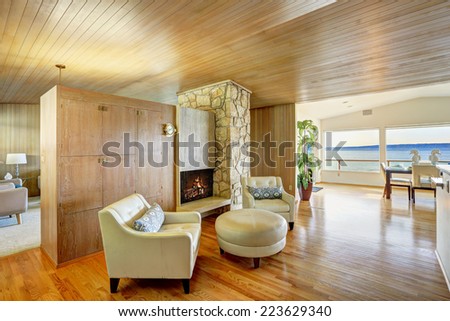 Luxury house interior. Sitting area with leather armchairs and leather ottoman. Cabinet with fireplace and rock wall trim