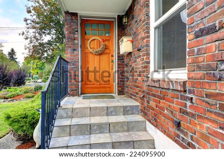 House exterior with brick trim. Entrance porch with orange door and staircase