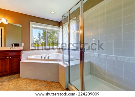 Bathroom interior with corner bath tub and screened shower. Tile floor and white tile wall trim