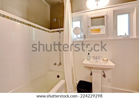 Simple bathroom interior with washbasin stand and bath tub. Dark brown wall with white tile trim and plank panel trim