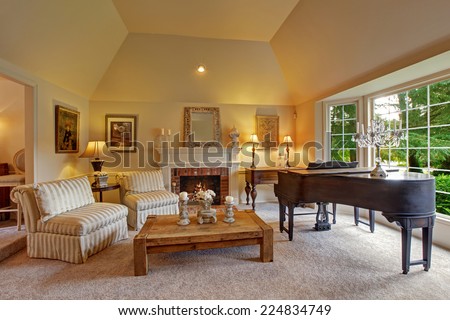 Luxury family room with high vaulted ceiling and large french window. Room has grand piano, fireplace, striped chairs and wooden coffee table