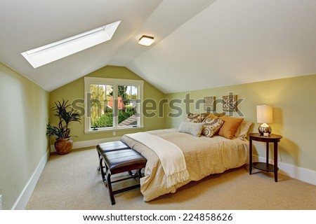 Light mint bedroom interior with white vaulted ceiling and skylight. Room has queen size bed, ottoman and table