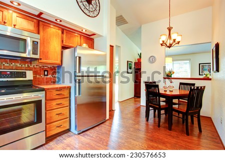 Kitchen room with orange tile back splash trim, maple cabinets and steel appliances. Dining area with high ceiling and wooden table set