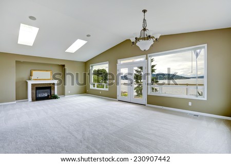 Empty spacious living room with walkout deck and fireplace. Room with high vaulted ceiling and skylights.