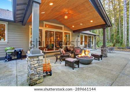 Large back yard with grass and covered patio with fire pit.