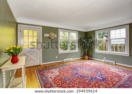 Large front room with chic decor, red rug, and green walls.