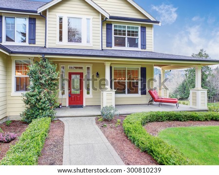 Classic american home with yellow exterior, and blue trim. also a red door.