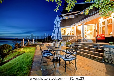 Luxury house exterior with impressive water view and cozy patio area. Summer evening.