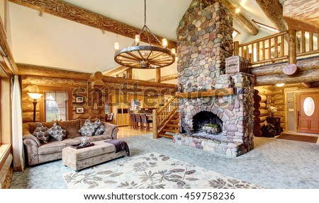 Bright Living room interior in American log cabin house. Rustic chandelier, stone fireplace and high ceiling with wooden beams make room gorgeous. Northwest, USA