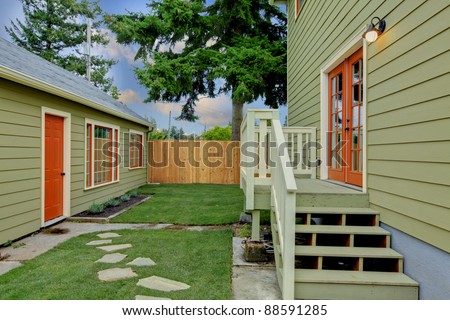 Green house with orange doors and detached guest house in the back yard