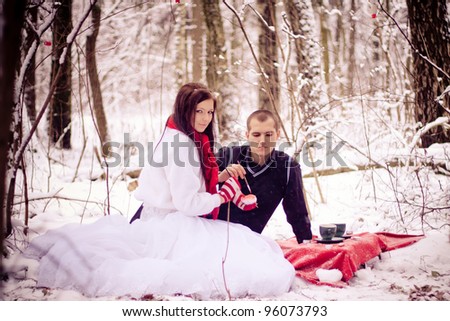 Beautiful couple in love drinks tea in the snow forest.