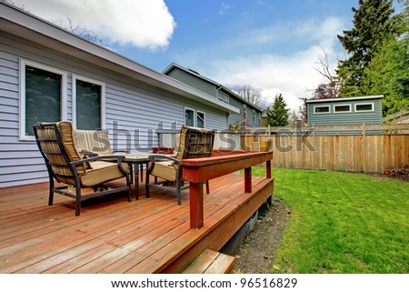 One story grey house deck with outdoor furniture and fenced back yard.