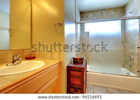 Bathroom with tub behind modern glass, stone tile, and white sink in a wood cabinet.