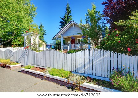 Charming old cute grey house behind the white fence with flowers.