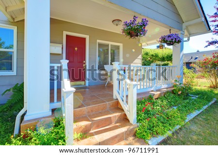 Grey house porch with red door, white railings and purple flowers.