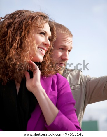 Happy couple outside wearing  light jackets. Man is showing something at the distance.