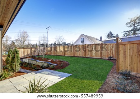 Sloped backyard surrounded by wooden fence. Exterior of New Luxury  home with tiled walkway and green lawn. Northwest, USA