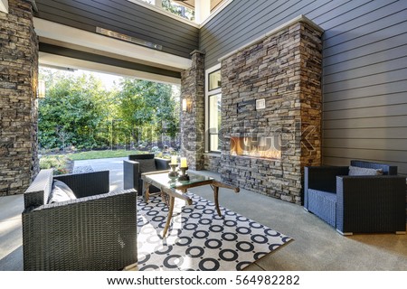 Well designed covered patio boasts stone fireplace, wicker patio chairs facing gorgeous rustic wood coffee table atop white and black geometric rug. Northwest, USA