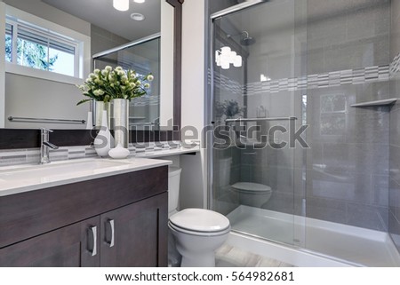 Bright new bathroom interior with glass walk in shower with grey tile surround, brown vanity cabinet topped with white counter and paired with mosaic tile backsplash. Northwest, USA
