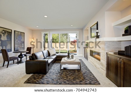 Cozy living room space with wet bar nook. Furnished with black leather sofa facing rectangular upholstered ottoman placed in front of traditional fireplace. Northwest, USA