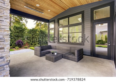 New modern home features a backyard with covered patio accented with stone fireplace, vaulted ceiling with skylights and furnished with gray wicker sofa placed on concrete floor. Northwest, USA