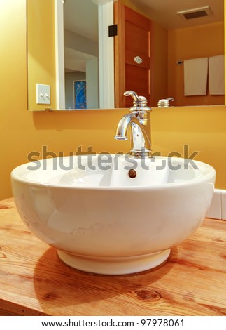 Round white sink with faucet and natural pine wood.