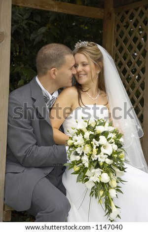 Bride and groom embrace affectionately on arbor seat, UK.