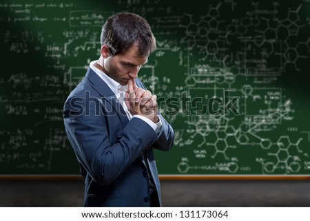 A Teacher , scientist or College Professor standing and thinking in front of a chalkboard with complex mathematical equations.