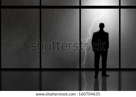 Business Man in high rise office looking out at a lightning storm
