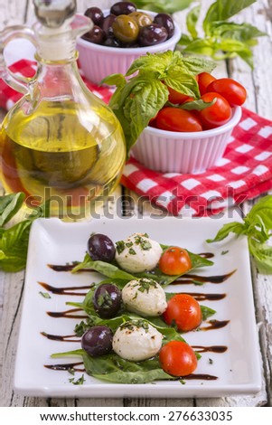 Caprese Salad with olive oil and balsamic vinegar on a white plate and a rustic wooden table