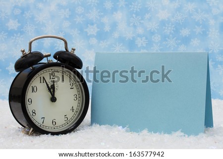 An old-fashion alarm clock with a blank blue card on snow and a blue snowflake background, It is Christmas Time