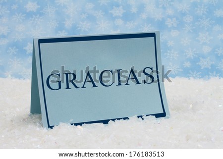 Gracias Thank You Message, A blue blank card on snow and a blue snowflake background with text of Gracias