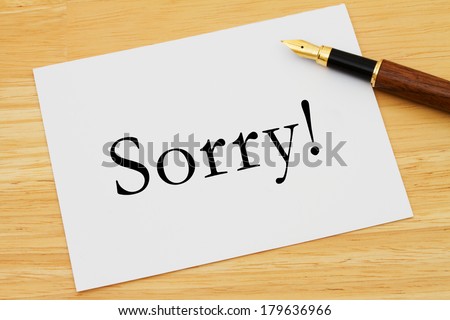 A white card with text of sorry and a fountain pen on a wooden desk, Saying your sorry