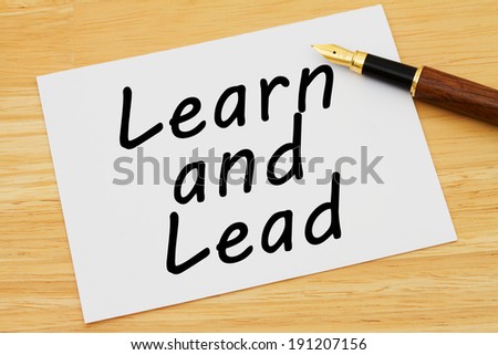 Learn and Lead, A white card with text of Learn and Lead and a fountain pen on a wooden desk
