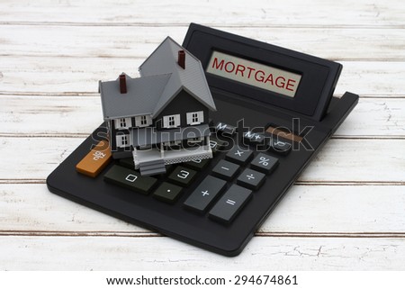 Calculating your mortgage payments, A gray model house on a calculator with word Mortgage over a distressed wood background