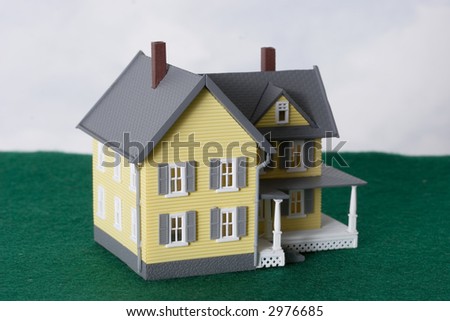 two story yellow house on green and blue background with copy space