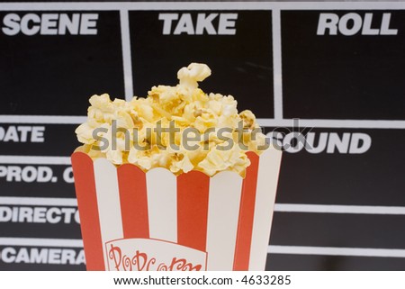 Popcorn in a red and white popcorn bag with a movie action board background