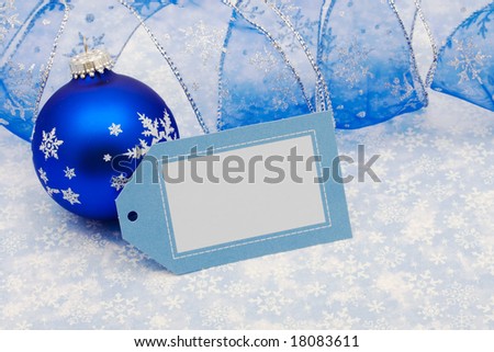 Blank gift tag with blue ribbon and glass ball on blue snowflake background, merry Christmas