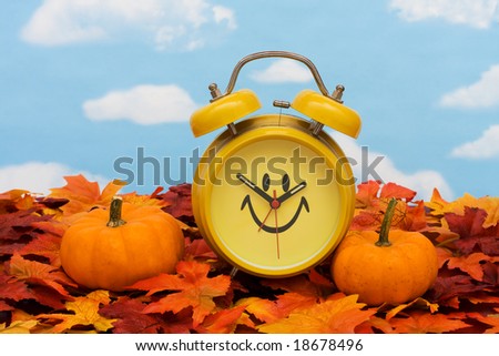 Fall leaves with yellow clock and pumpkins on sky background, fall back time change