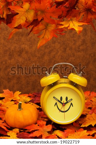 Fall leaves with yellow clock and pumpkin on brown background, fall back time change