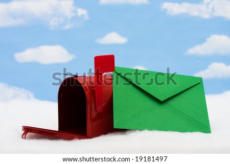 Red mailbox with the flag up sitting on snow with green envelope and a sky background, mailbox