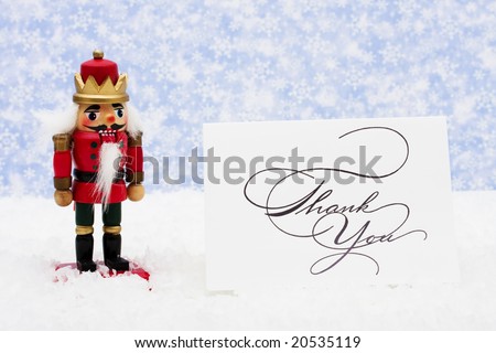 Nutcracker sitting on snow with thank you card on a snowflake background, nutcracker