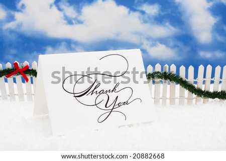 Thank you card sitting on snow with white fence and green garland on a sky background, nutcracker