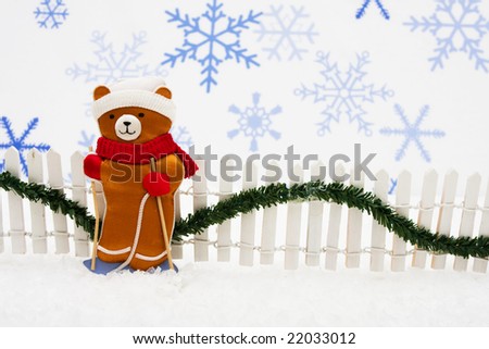 Stuffed bear with white fence and green garland on snowflake background, Christmas bears