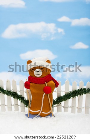 Stuffed bear with white fence and green garland on sky background, Christmas bears
