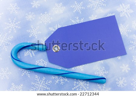 Blue candy cane with a blank gift tag sitting on a blue snowflake background, candy cane